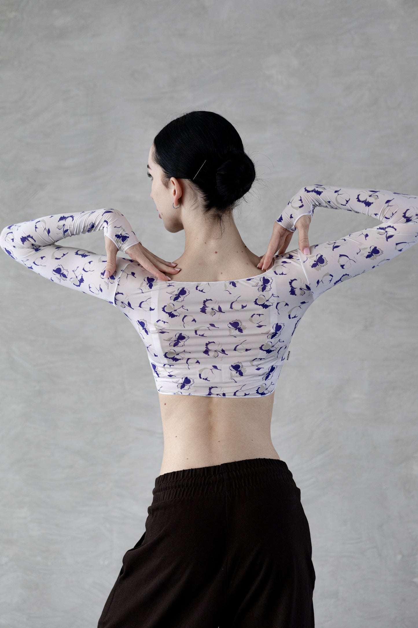 Dancer wearing a white Dancelab crop top with blue patterns and black pants against a gray background