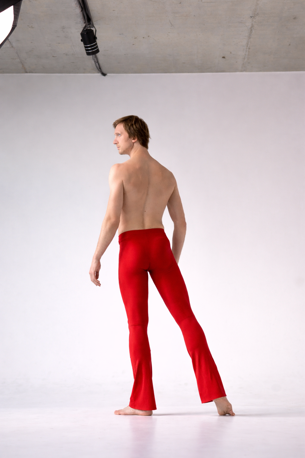 Man wearing red pants for ballet standing against a white background