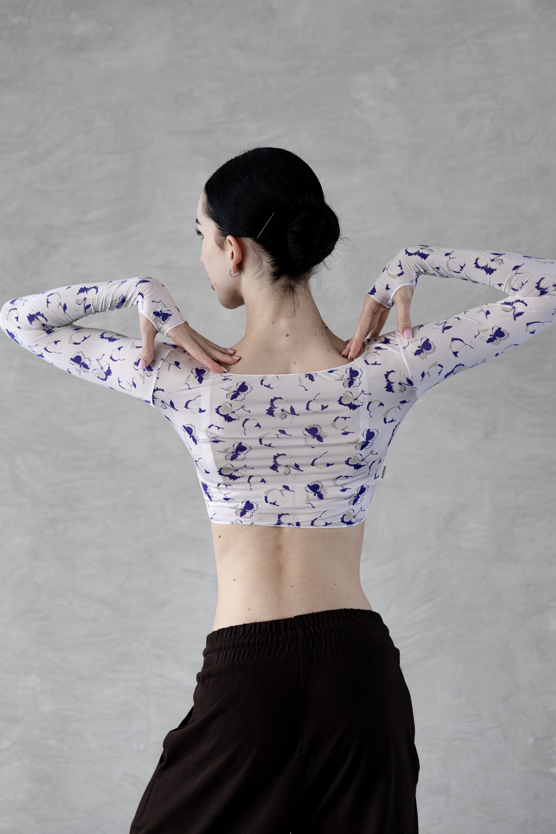 Dancer wearing a white Dancelab crop top with blue patterns and black pants against a gray background