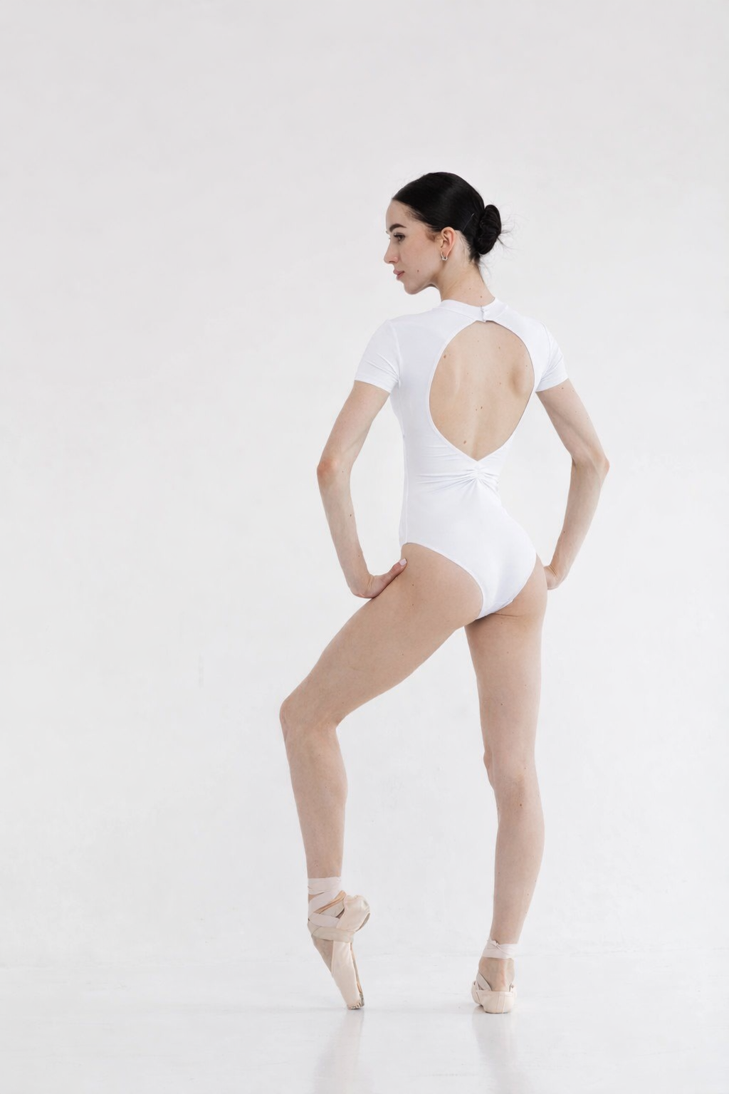 Ballerina in a white leotard with open back on a white background