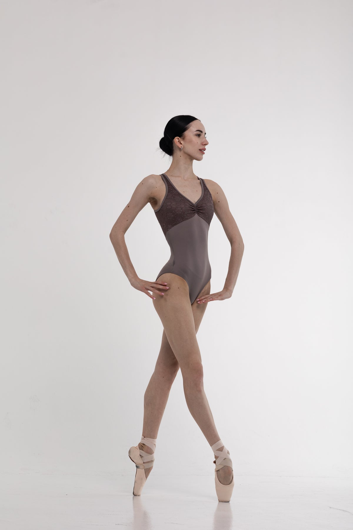 Ballerina in a brown ballet leotard and beige tights on a white background
