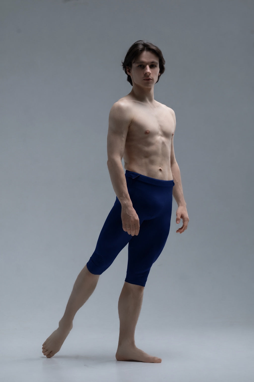 Ballet dancer wearing short blue tights against a gray background