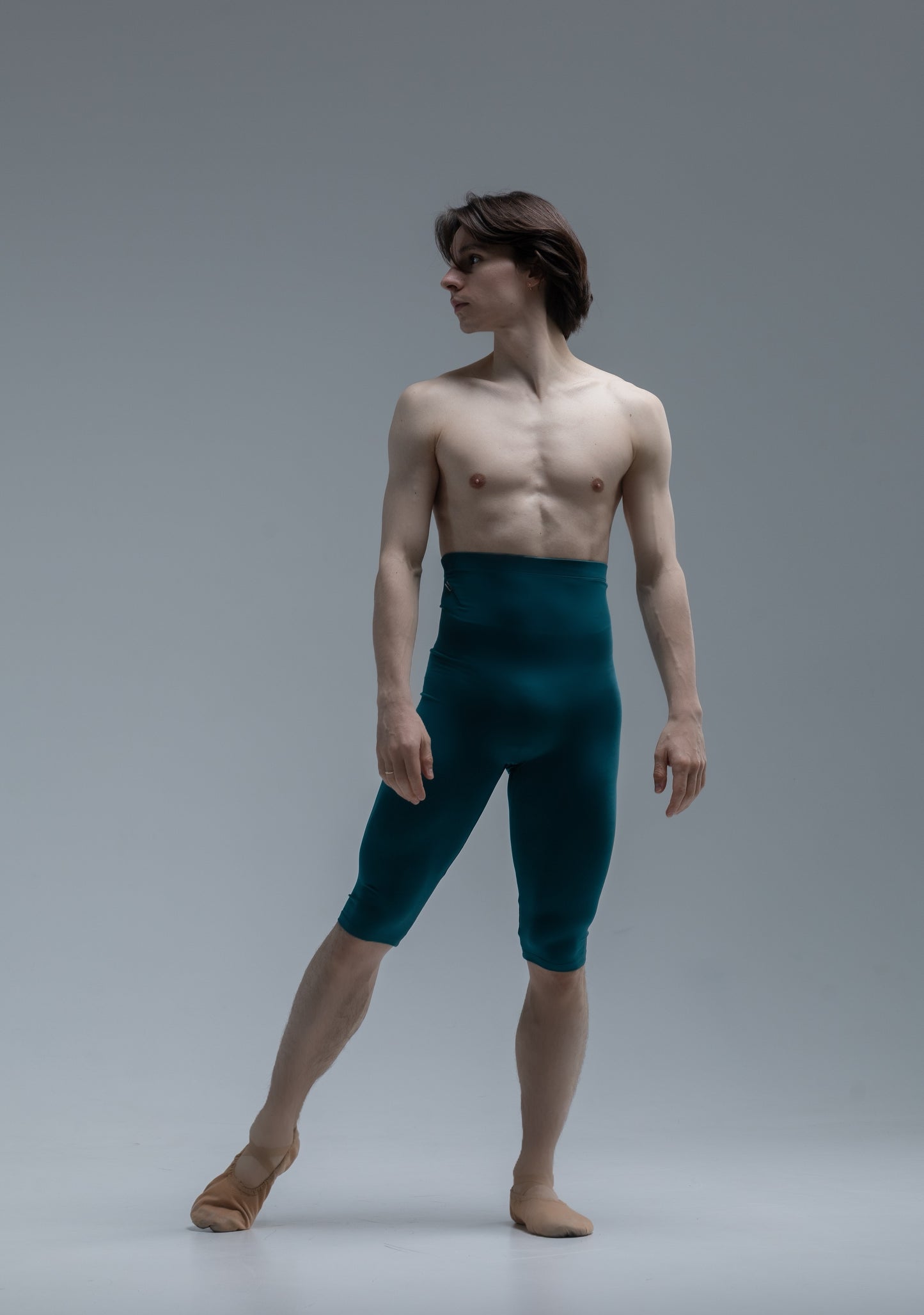 Ballet dancer in teal tights and beige shoes on a gray background