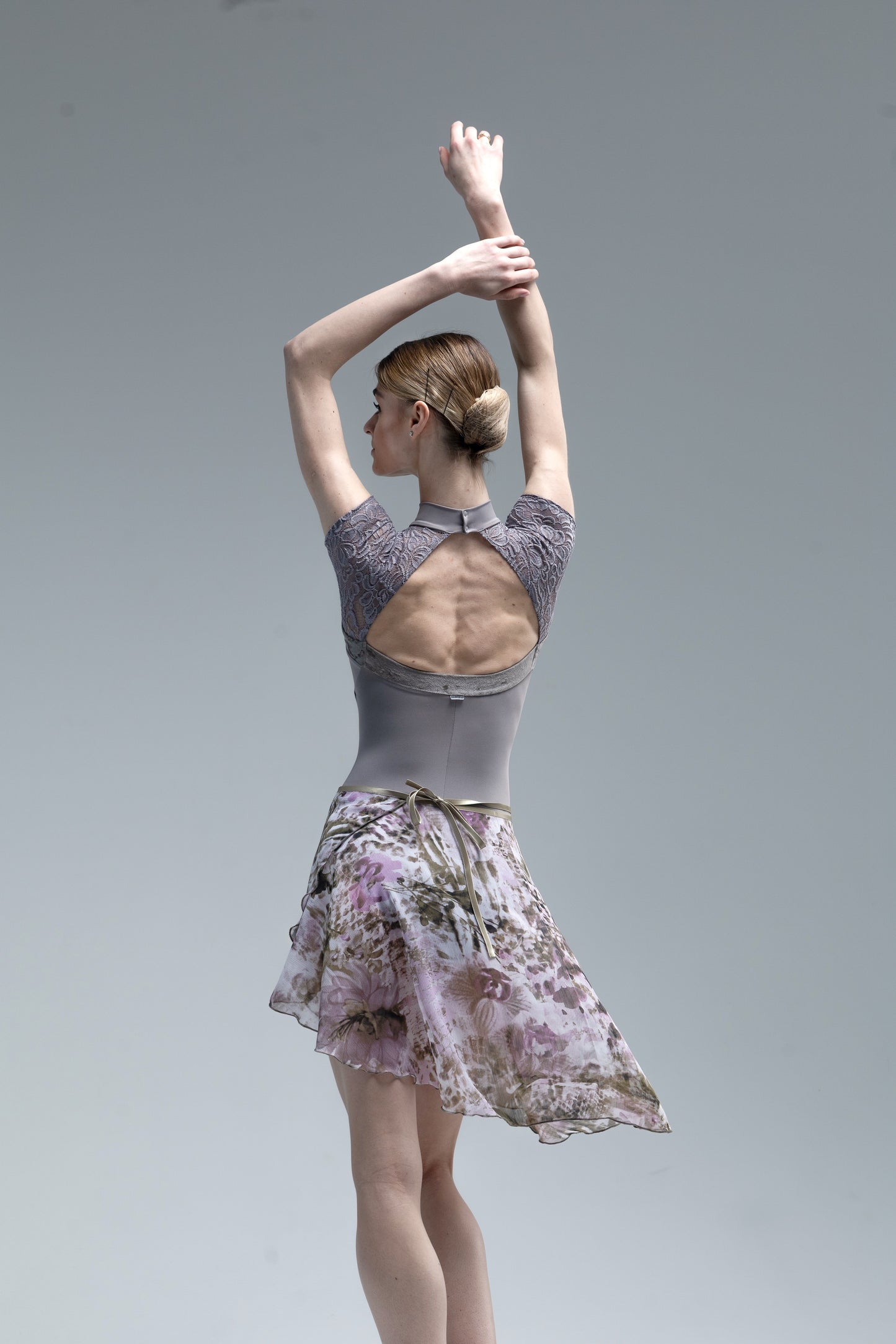 Dancer in a floral skirt and open-back top against a plain background
