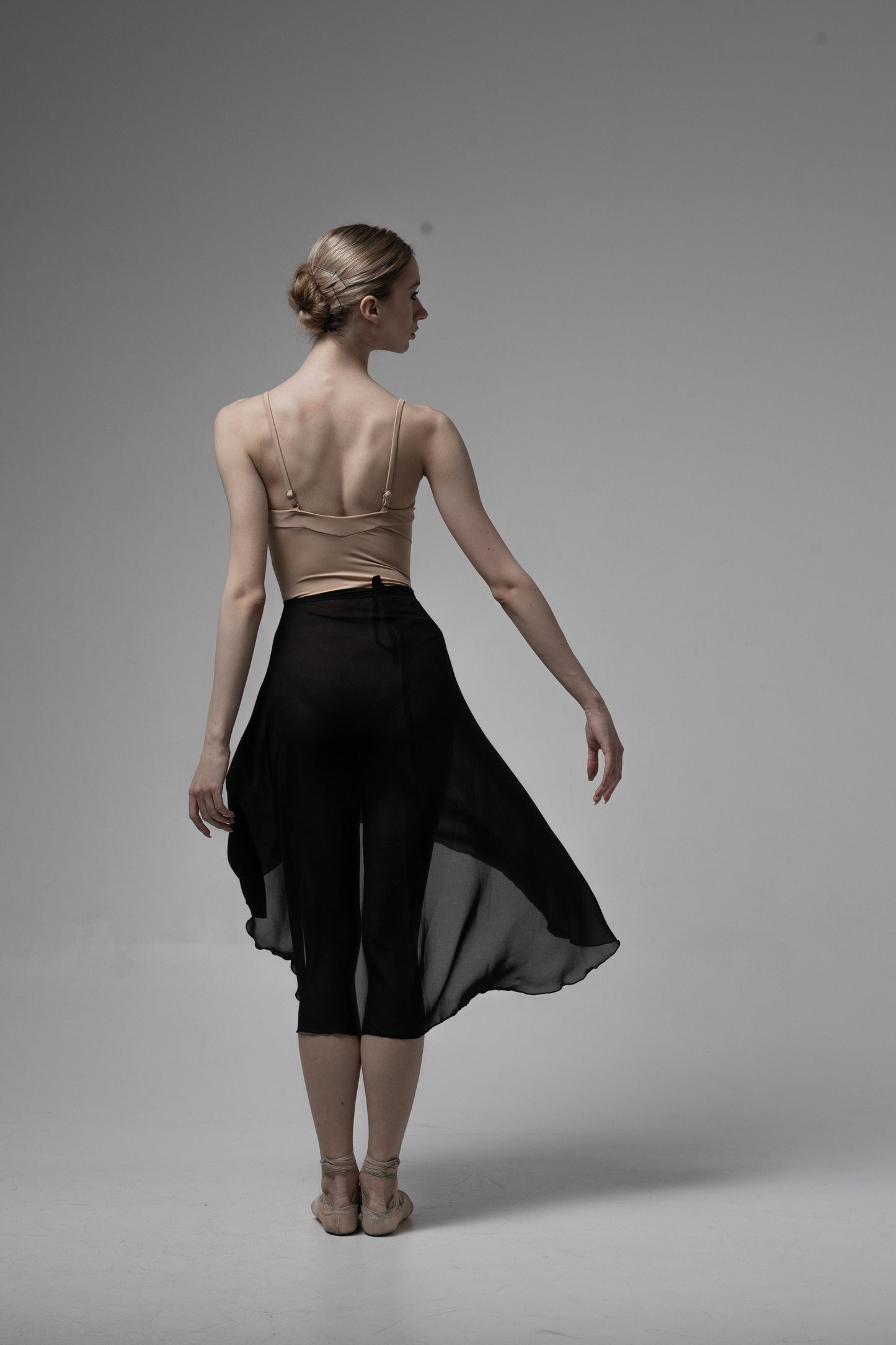 Dancer in a black skirt an leotard nude color for ballet on a gray background