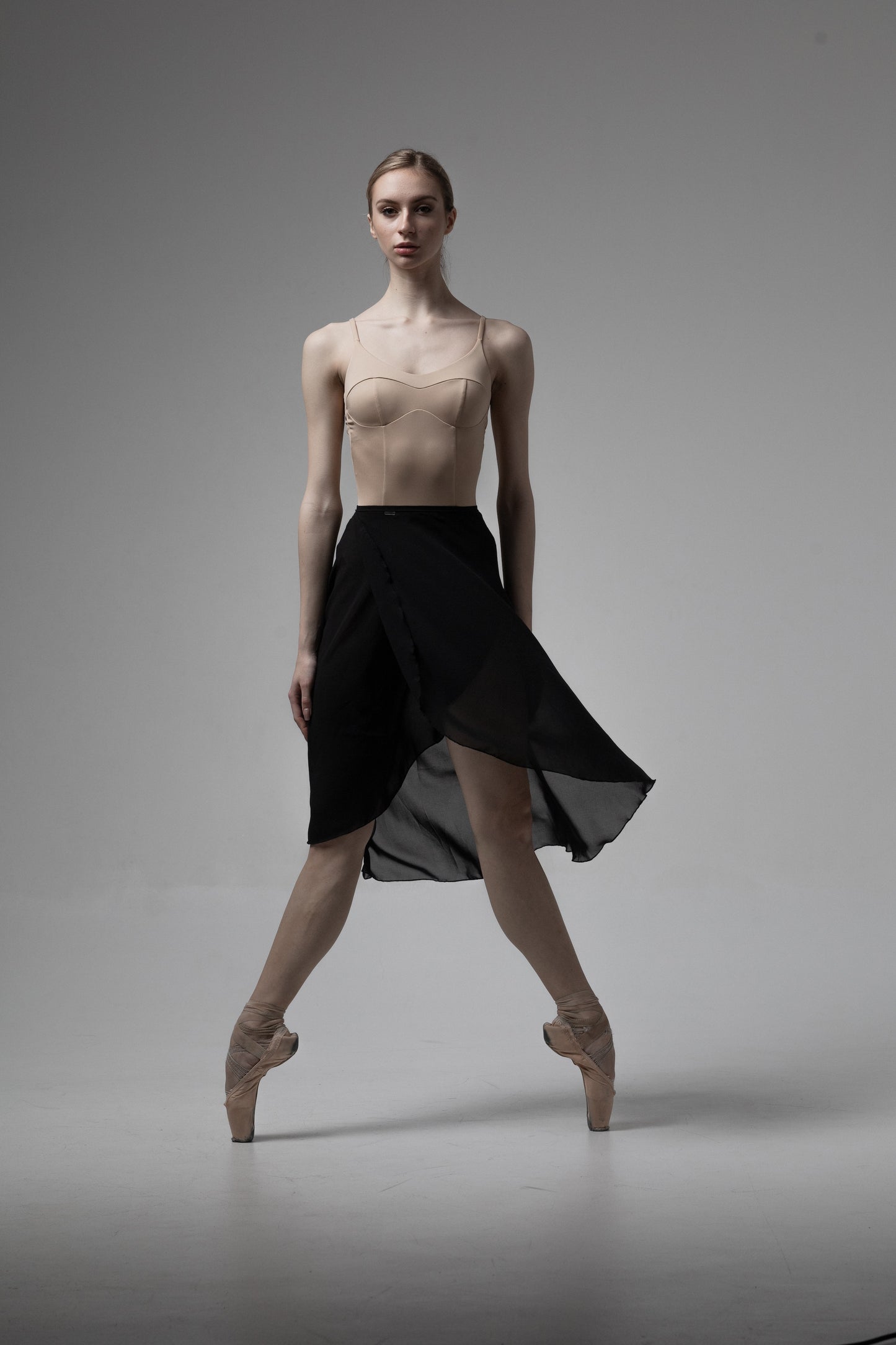 Ballerina in a black skirt and Leotard nude color on a gray background