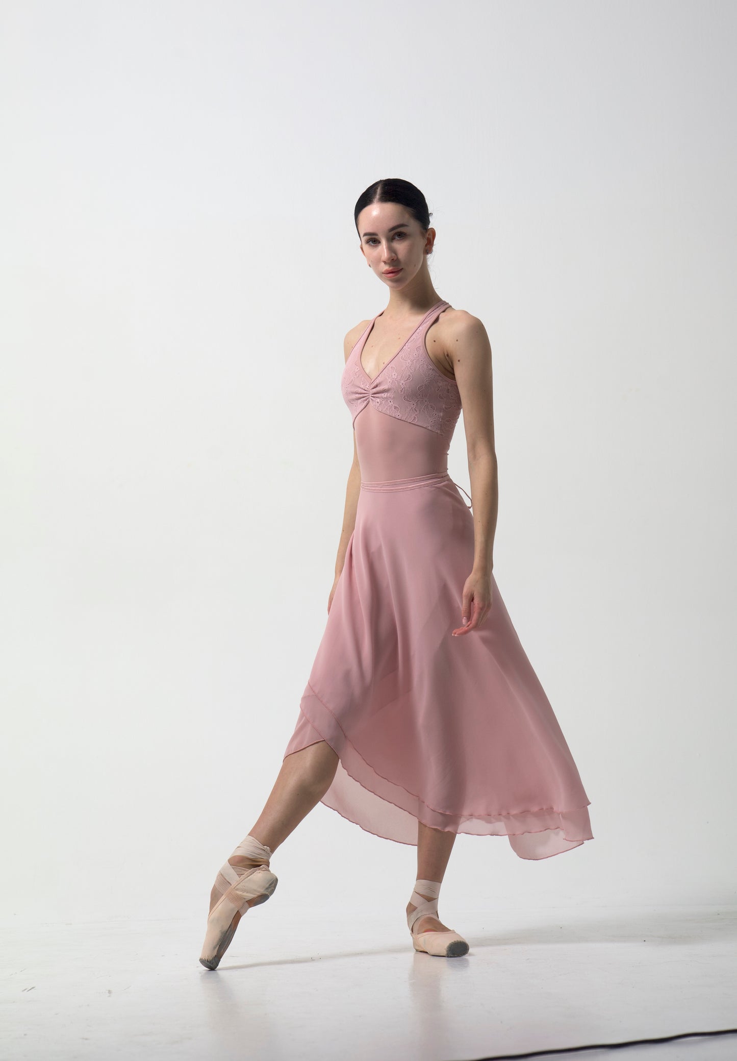 Dancer in a pink skirt and leotard posing on a white background