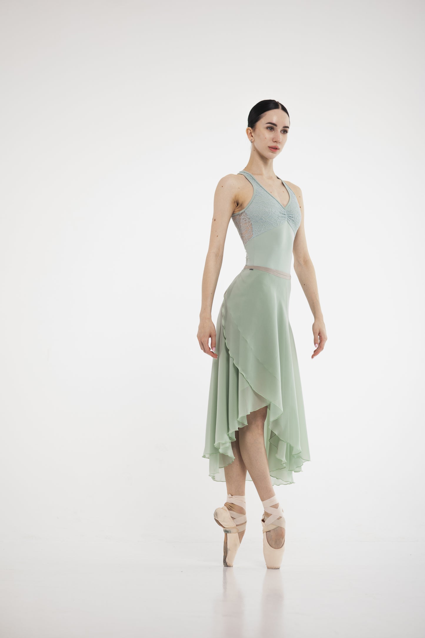 Ballerina in a pistachio skirt, leotard and ballet shoes on a white background